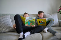 Two children sitting on a couch reading books together.