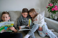 Three children sitting on a couch reading books in a cozy living room.
