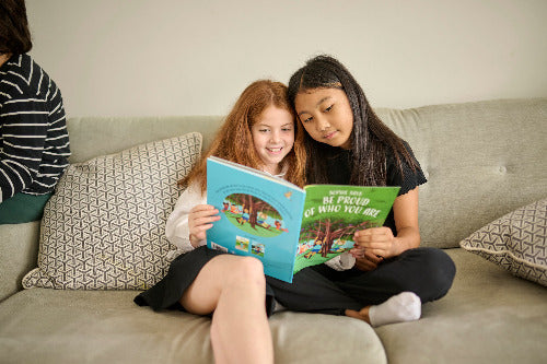 Two young girls sitting on a couch reading a book together.