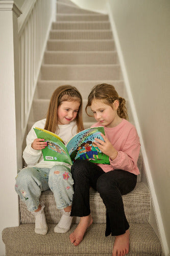 Two young girls sitting on a staircase reading a book together.
