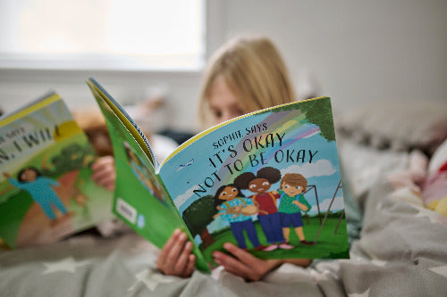 Person reading a book titled 'Not to be Okay' to a child in bed.