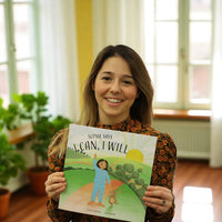 Esther holding a book titled 'I Can, I Will' in a room with plants and windows.